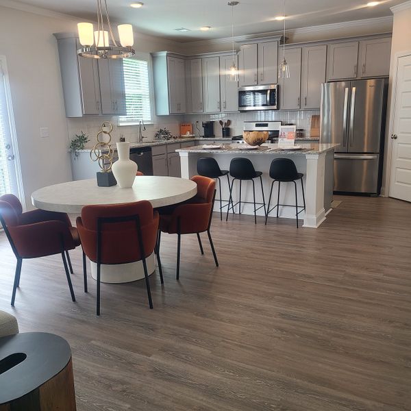 A modern kitchen with gray cabinets, sleek appliances, and a round dining table complemented by stylish rust-colored chairs.