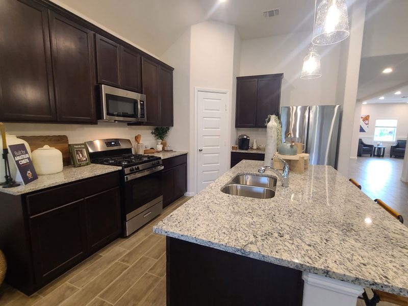 A modern kitchen with dark cabinetry, granite countertops, stainless steel appliances, and pendant lighting. A modern kitchen with dark cabinetry, granite countertops, stainless steel appliances, and pendant lighting.