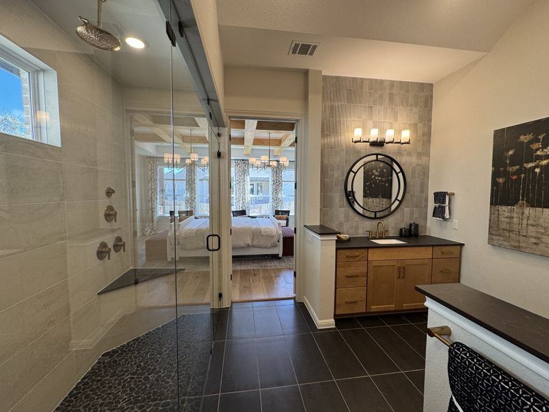 A luxurious bathroom featuring a glass-enclosed shower, sleek vanity, and elegant wall lighting, leading into a cozy bedroom.