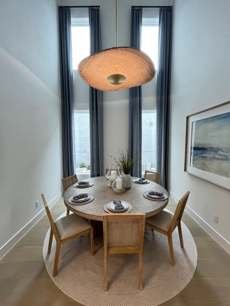 A dining area with a round wooden table, woven chairs, tall curtains, and a unique pendant light. A dining area with a round wooden table, woven chairs, tall curtains, and a unique pendant light.