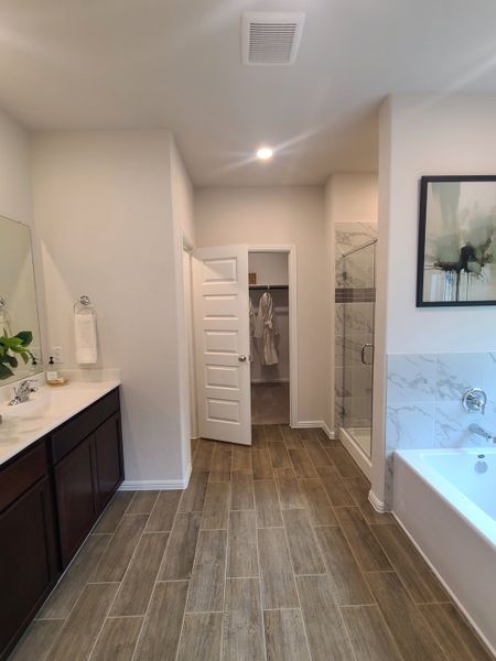 A modern bathroom with wood-look tile, dark vanity, glass shower, and relaxing bathtub. A modern bathroom with wood-look tile, dark vanity, glass shower, and relaxing bathtub.