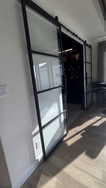 A modern interior with sleek black-framed glass sliding doors, wooden floors, and abundant natural light.