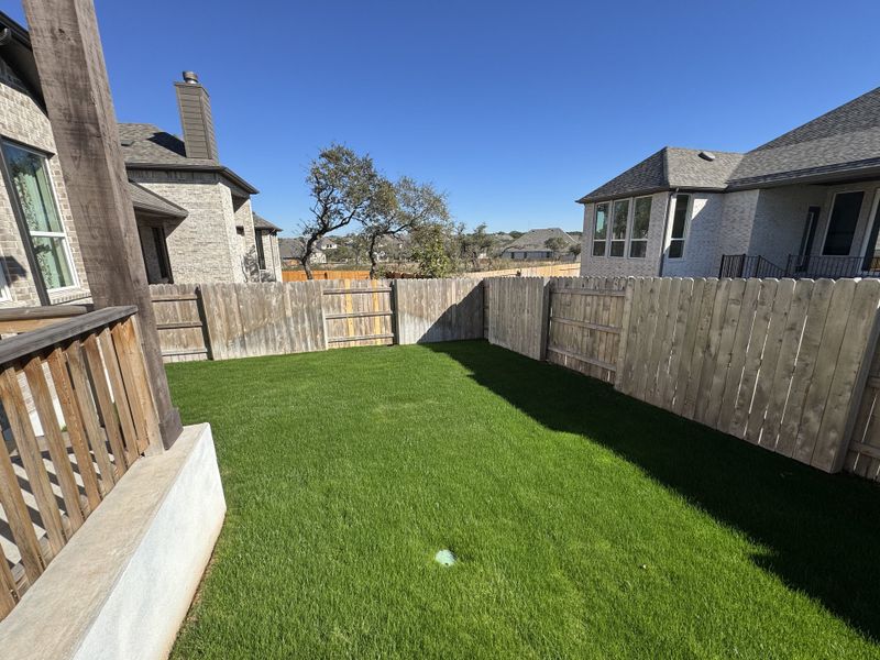 A charming backyard with lush green grass and a wooden fence in The Cottages at La Cima by Ashton Woods (San Marcos, TX).