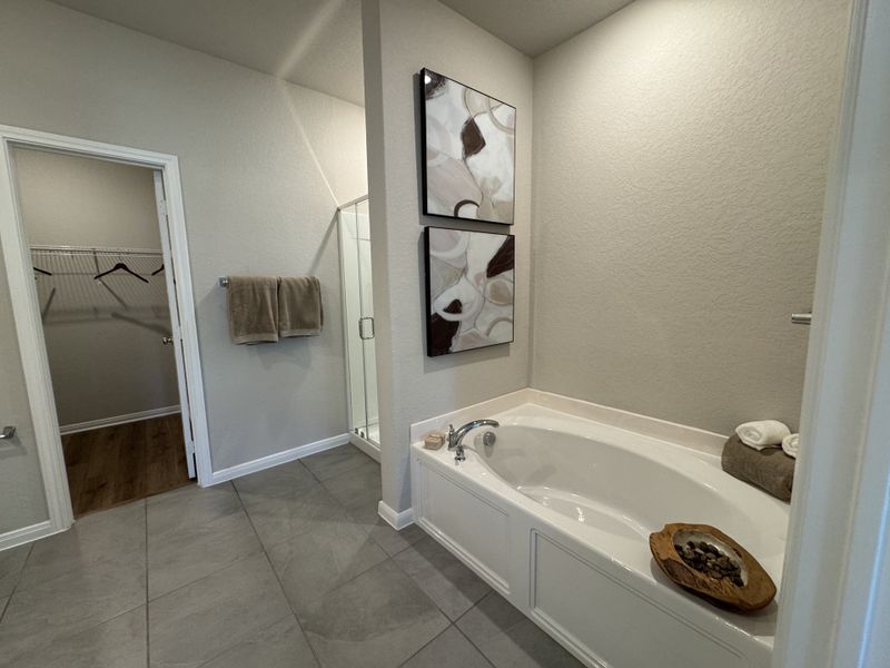 A modern bathroom with a large tub, abstract art, and a nearby walk-in closet, creating a serene retreat.
