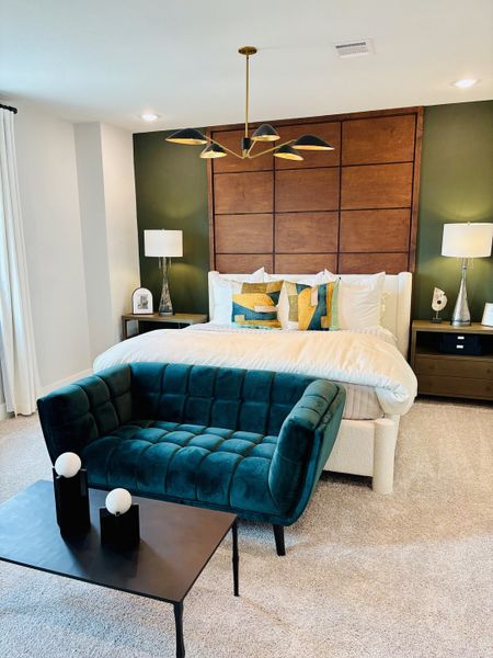 A modern bedroom with an elegant green accent wall, plush velvet loveseat, and contemporary lighting.