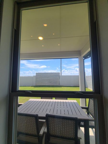 A cozy patio view with a stylish outdoor table, sheltered under a ceiling and open to a lush green backyard. A cozy patio view with a stylish outdoor table, sheltered under a ceiling and open to a lush green backyard.