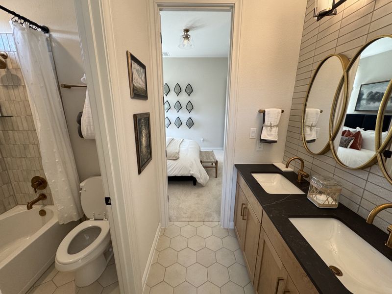 A chic bathroom with a double vanity, hexagon tiles, and a view into a cozy, well-decorated bedroom.