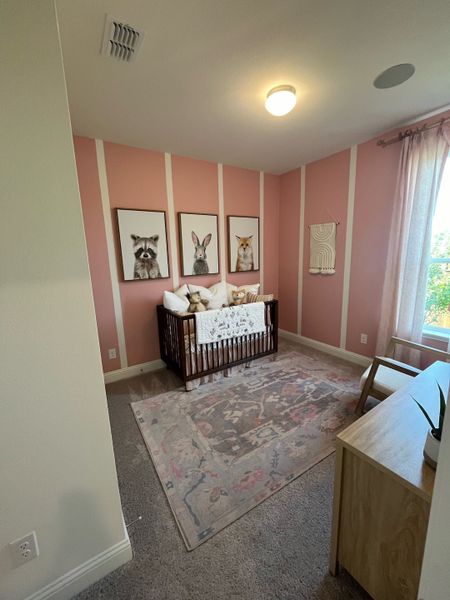 A cozy nursery with pink walls, charming animal art, a wooden crib, and a soft patterned rug.