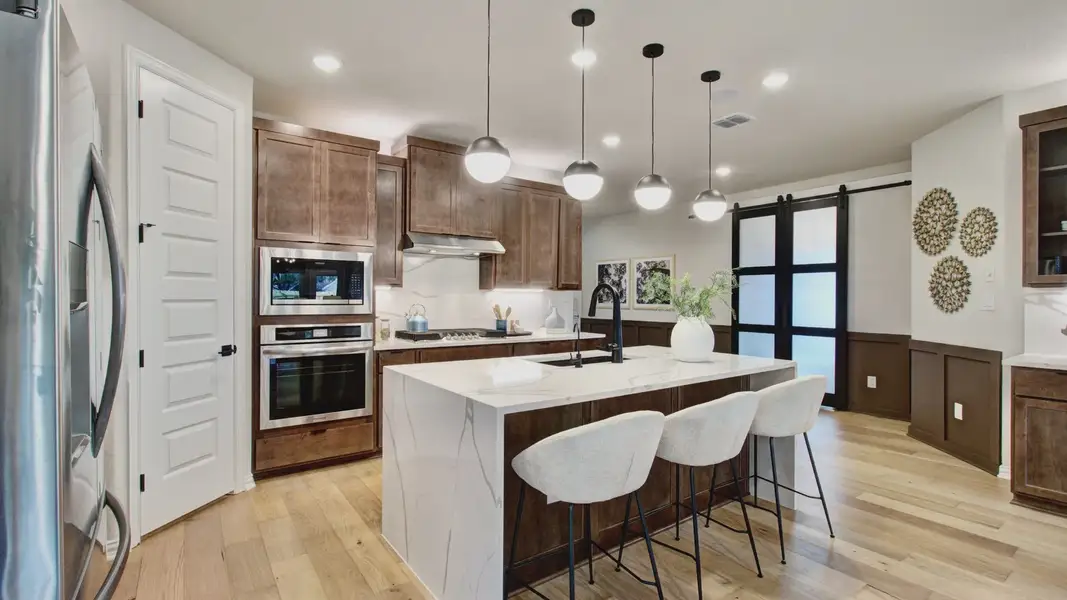 Elegant kitchen features pristine marble island, rich wood cabinetry, and ambient pendant lighting in Sunflower Ridge.