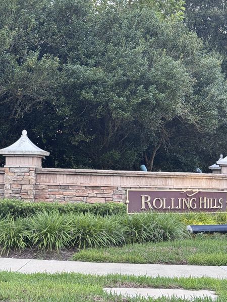 Elegant entrance with lush greenery and a stone sign in Shadow Crest at Rolling Hills by Adams Homes (Green Cove Springs, FL).