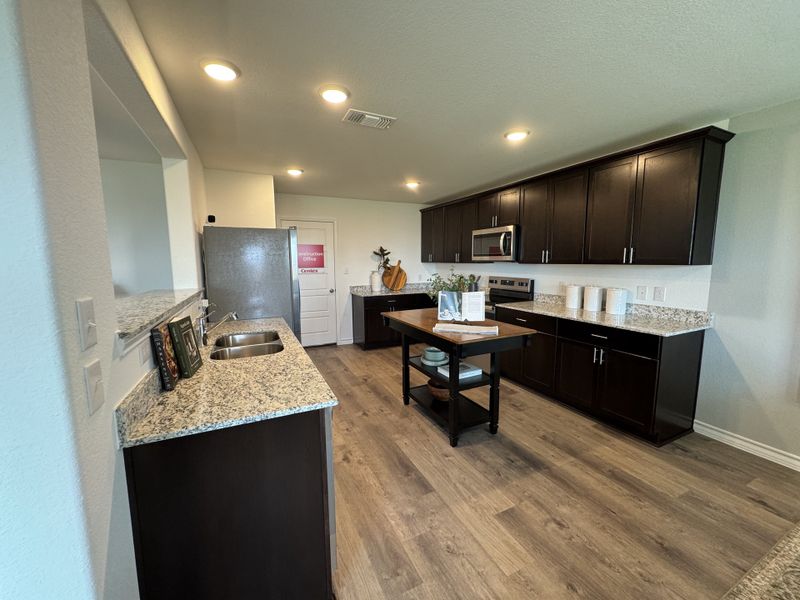 A modern kitchen with dark cabinetry, granite countertops, and wood-look flooring, offering a sleek and functional design.