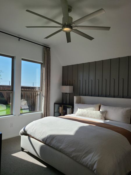 A cozy bedroom with a modern ceiling fan, large windows, and stylish paneling behind the bed. A cozy bedroom with a modern ceiling fan, large windows, and stylish paneling behind the bed.