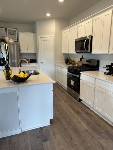 A modern kitchen featuring white cabinetry, stainless steel appliances, and elegant wood flooring.