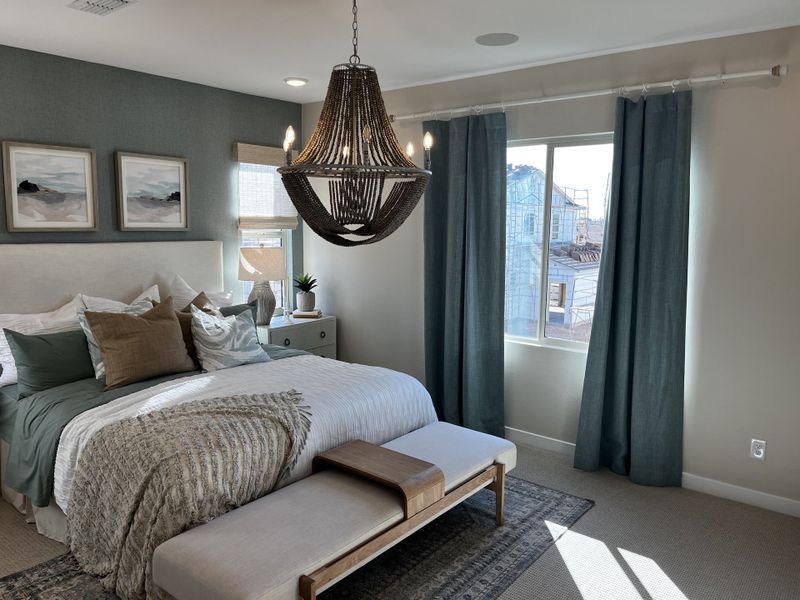 Cozy bedroom with a luxurious chandelier, teal curtains, and plush bedding in neutral tones with a bench at the foot.