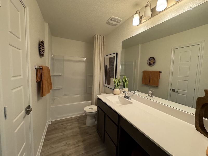 A contemporary bathroom with sleek dark cabinetry, wood flooring, elegant lighting, and modern wall decor. A contemporary bathroom with sleek dark cabinetry, wood flooring, elegant lighting, and modern wall decor.
