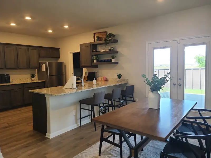 A modern kitchen with granite countertops, dark wood cabinets, and a cozy dining area with natural light from glass doors. A modern kitchen with granite countertops, dark wood cabinets, and a cozy dining area with natural light from glass doors.