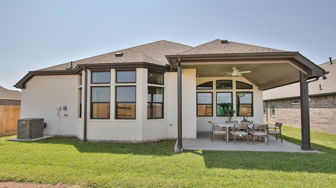 Spacious Sunterra residence features expansive windows and a refined, covered patio amid lush greenery.