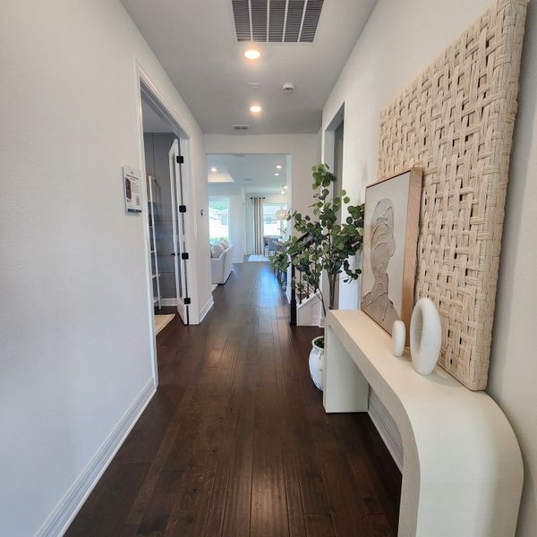 A modern hallway with elegant wood flooring, stylish decor, and soft lighting leading to an open living space.