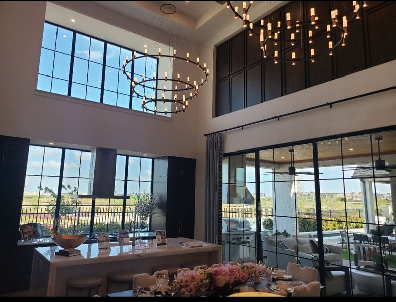A spacious living area with high ceilings, elegant chandeliers, and expansive windows overlooking a scenic outdoor patio.