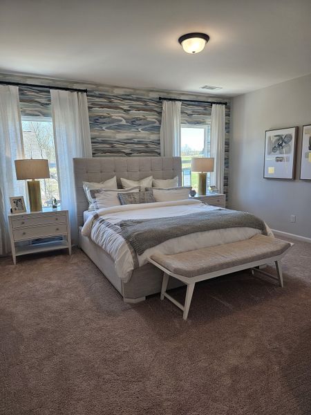 A serene bedroom featuring an upholstered bed, abstract wallpaper, cozy carpeting, and elegant decorative accents.