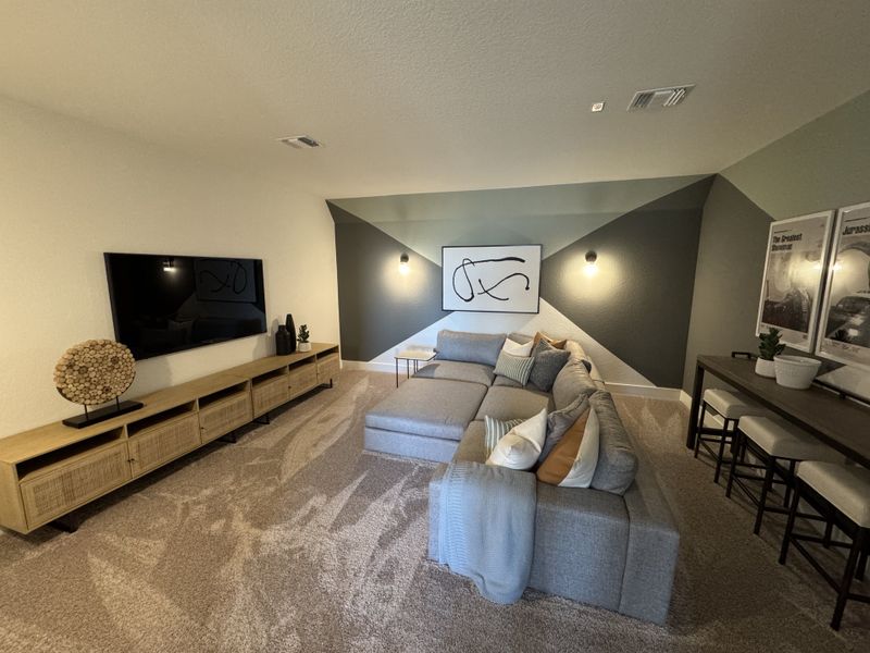 A cozy living area with a modern sectional sofa, geometric accent wall, and stylish entertainment setup.