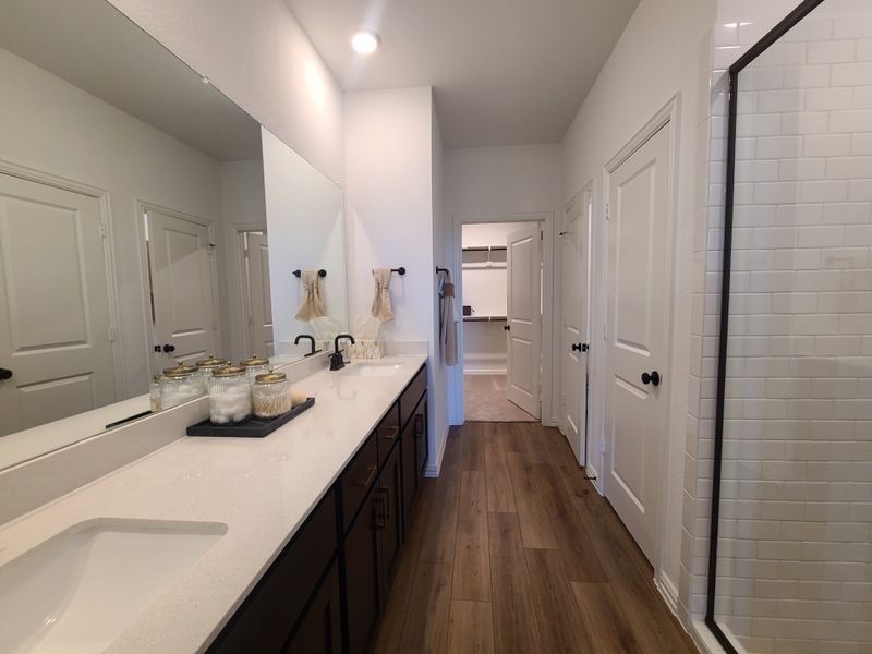 A modern bathroom with dual sinks, a large mirror, wood flooring, and a spacious walk-in shower. A modern bathroom with dual sinks, a large mirror, wood flooring, and a spacious walk-in shower.