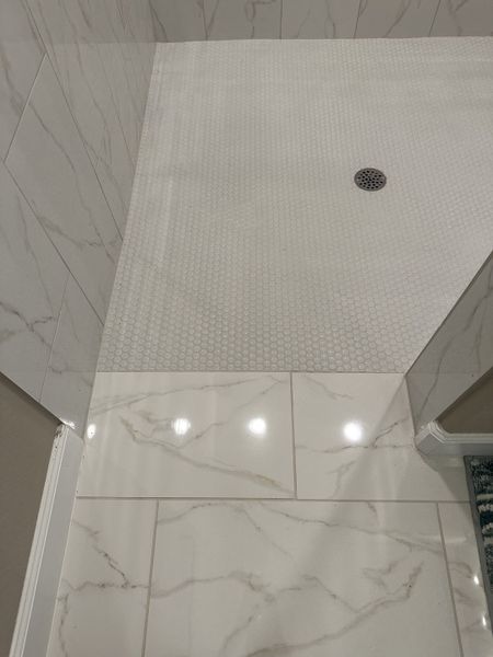 A modern shower with sleek marble-tiled walls and a textured hexagonal floor drain design. A modern shower with sleek marble-tiled walls and a textured hexagonal floor drain design.