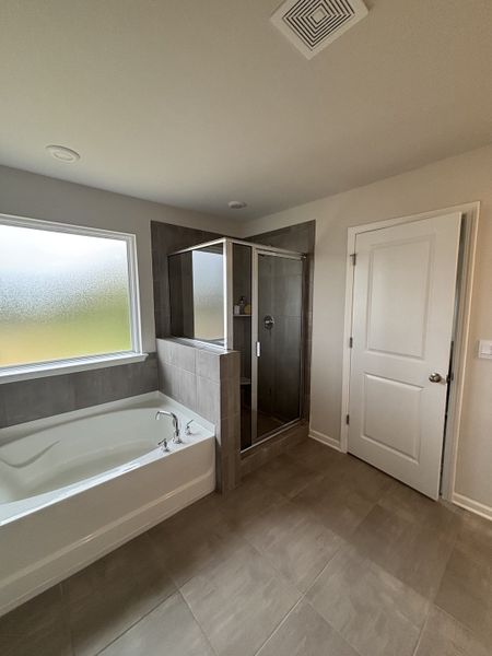 A modern bathroom with a spacious bathtub, glass-enclosed shower, and light tile flooring.