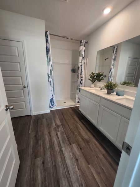 A modern bathroom with sleek wood flooring, a large vanity, and a bright shower area featuring patterned curtains.