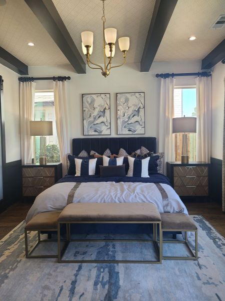 A luxurious bedroom featuring a vaulted ceiling, elegant chandelier, stylish bedding, and modern art pieces above the headboard.