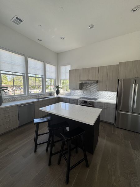 A modern kitchen with sleek cabinets, island seating, stainless appliances, and ample natural light through large windows. A modern kitchen with sleek cabinets, island seating, stainless appliances, and ample natural light through large windows.