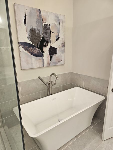 A chic bathroom features a sleek freestanding tub, abstract art, and modern fixtures, creating a serene atmosphere.