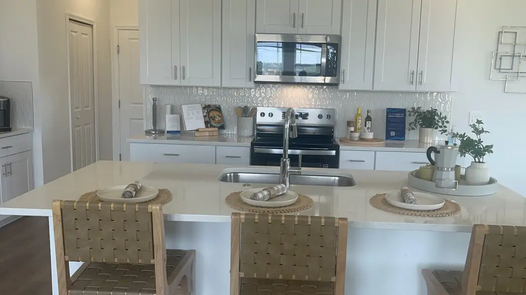 A modern kitchen with sleek white cabinets, stainless steel appliances, and a chic island with woven stools.