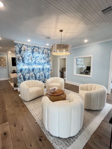 A cozy seating area with plush white chairs, a rattan coffee table, and a tropical accent wall under warm lighting.