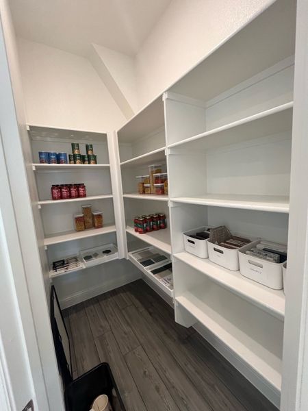 A spacious pantry with sleek white shelving, neatly organized with jars and boxes, on elegant wood flooring.