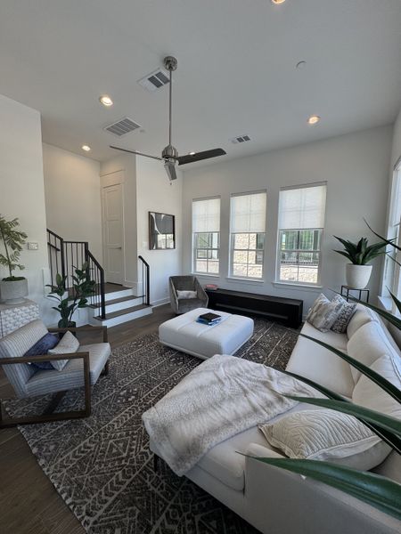 A modern living room featuring a light sofa, patterned rug, and ceiling fan with natural light streaming through ample windows. A modern living room featuring a light sofa, patterned rug, and ceiling fan with natural light streaming through ample windows.