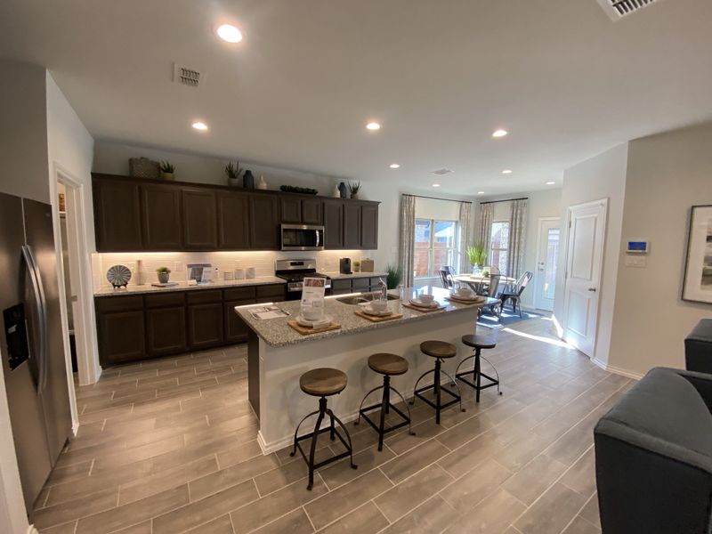A modern kitchen with dark wood cabinets, a granite island, and sleek stainless steel appliances, leading to a bright dining area.