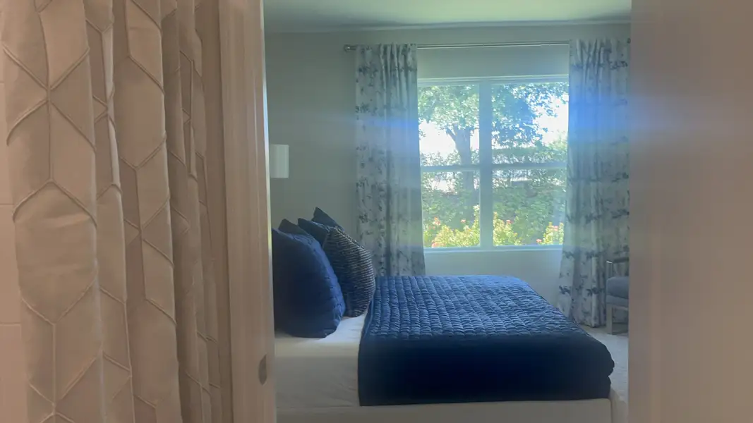 A cozy bedroom featuring a large window, soft lighting, elegant curtains, and a bed with plush navy bedding.