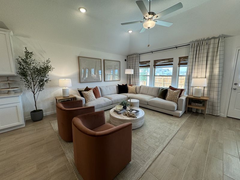 A cozy living room with a large sectional, velvet chairs, and elegant decor enhanced by natural light through wide windows.