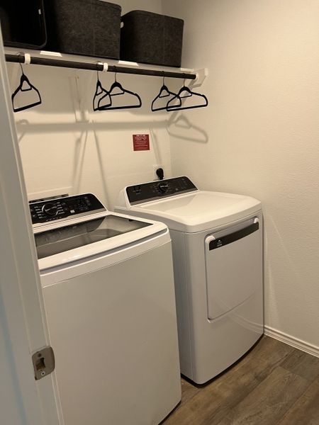A modern laundry room featuring a top-load washer, dryer, sleek shelving, and ample hanging space. A modern laundry room featuring a top-load washer, dryer, sleek shelving, and ample hanging space.