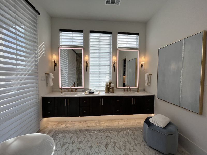 A luxurious bathroom with a long vanity, illuminated mirrors, elegant lighting fixtures, and stylish marble flooring.