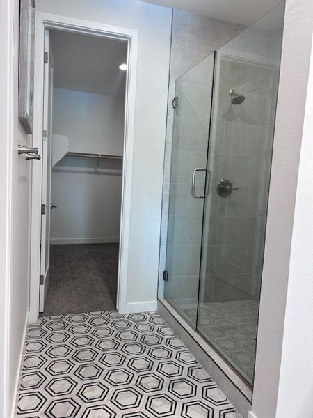 A bathroom with hexagonal tile flooring, a sleek glass shower, and a walk-in closet entry.