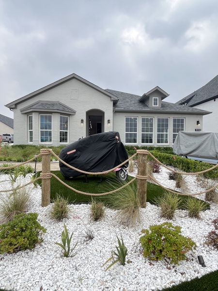 A charming white brick home with a landscaped yard in Bellagio by Megatel Homes (Forney, TX).
