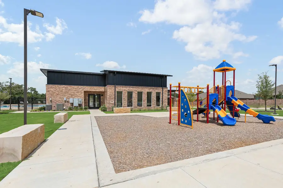 Community playground with slides and climbing structure next to brick clubhouse and pool area