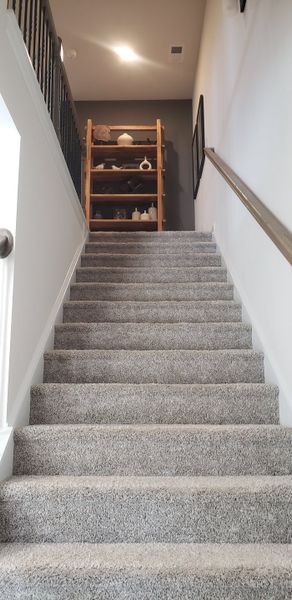 A carpeted staircase with modern railing leads to a wooden shelf filled with decorative pottery and art. A carpeted staircase with modern railing leads to a wooden shelf filled with decorative pottery and art.
