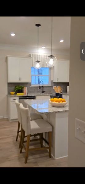 A modern kitchen featuring white cabinets, granite countertops, pendant lighting, and cozy seating at the island.