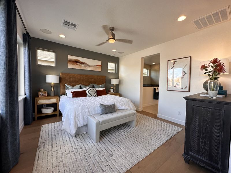 A modern bedroom with a cozy bed, elegant lighting, and stylish decor. Features gray accent wall and warm wood flooring.