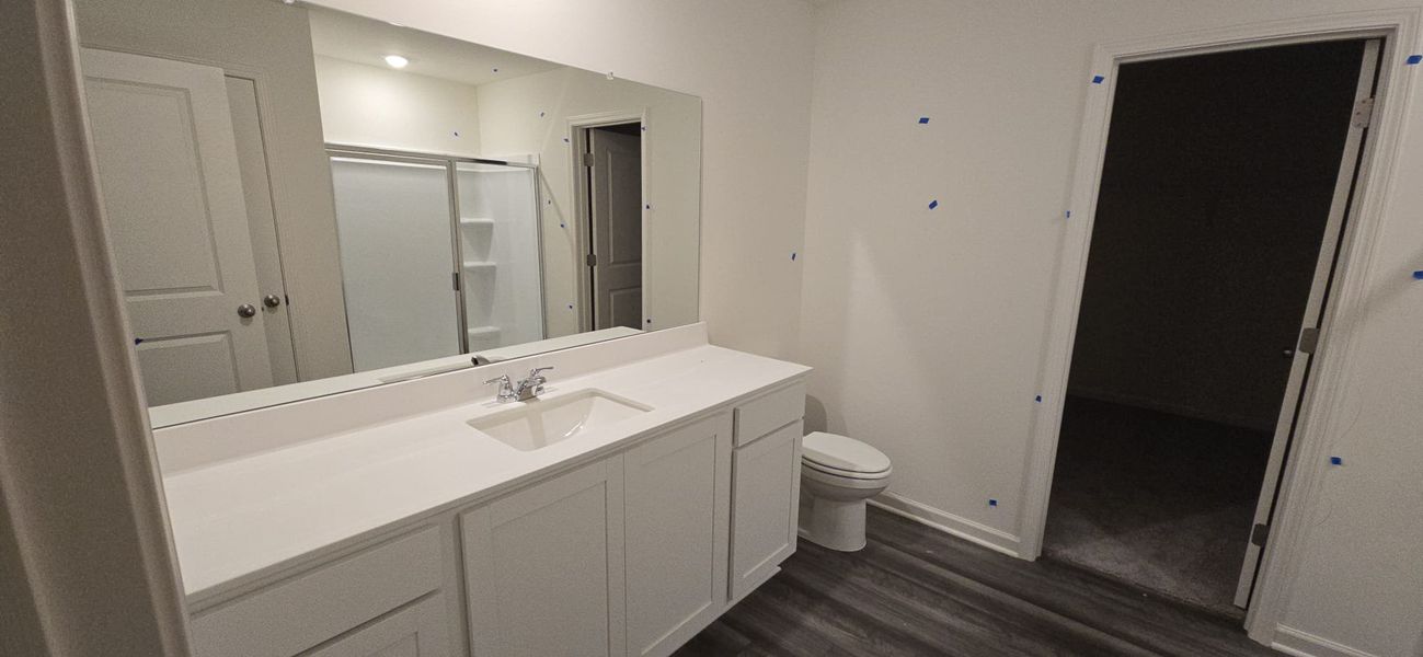 Modern bathroom with sleek white vanity, large mirror, and wood-look flooring.