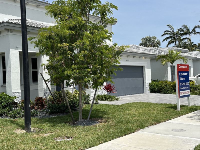A modern white home with a gray garage and lush landscaping in Salerno by Lennar (Richmond West, FL).