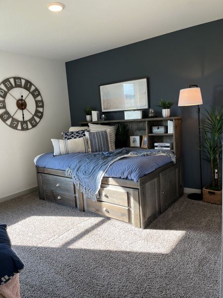 A cozy bedroom with a built-in wooden daybed, soft carpeting, and a navy accent wall adorned with stylish decor.